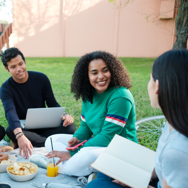 group sitting in grass with food and book and laptop